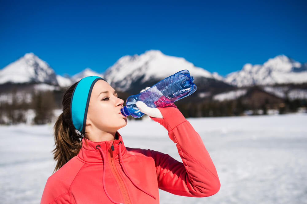 Woman in snow drinking water from bottle