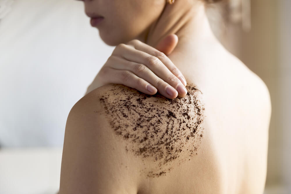 Woman using body scrub on back